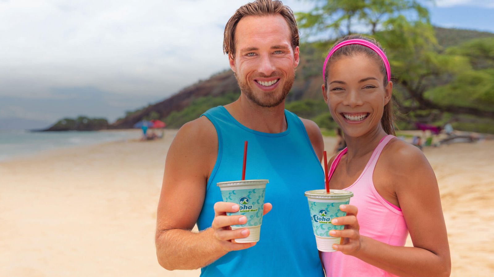 Couple smiling on beach with Aloha Islant Mart drinks